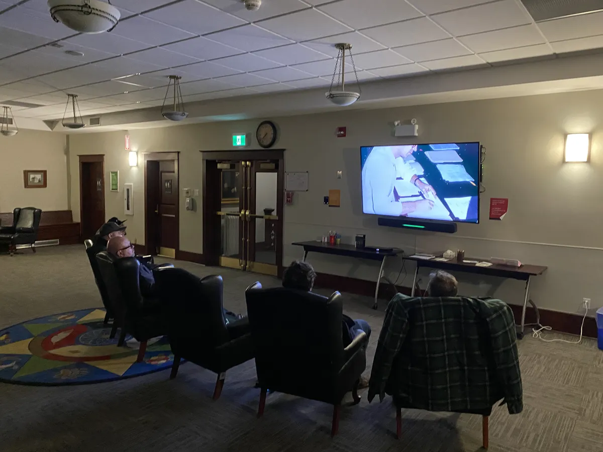 People in armchairs watching the General Magic documentary on a wall-mounted TV at the https://www.epl.ca/locations/eplstr/ library